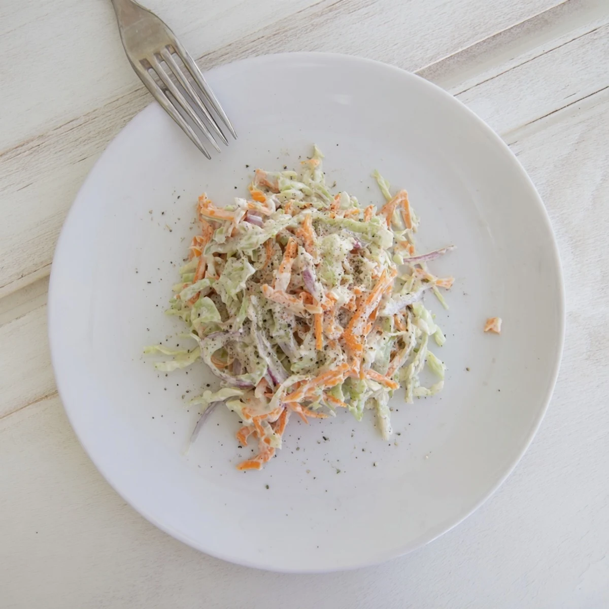 Freshly made Coleslaw with crisp green cabbage, shredded carrots, and creamy dressing in a white bowl.