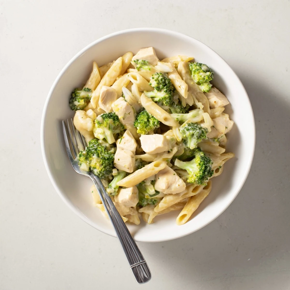 Tender penne pasta tossed with sautéed chicken, steamed broccoli, and a rich homemade cheddar cheese sauce in a white bowl.