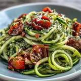Vibrant plate of spiralized zucchini with homemade pesto, cherry tomatoes, and Parmesan, an easy vegetarian Mediterranean dish.  