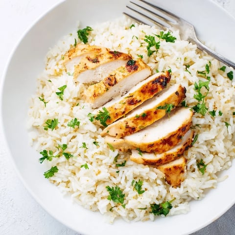 Fluffy garlic butter rice topped with juicy grilled chicken breast, garnished with fresh parsley and lemon wedges for a bright finish.