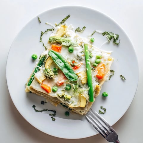 Freshly baked Spring Veggie Alfredo Lasagna emerges from the oven, showcasing golden bubbly mozzarella and layers of vibrant green asparagus and peas.