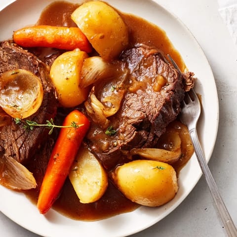Golden carrots and potatoes surrounding slow-cooked Beef Pot Roast on a rustic dinner table.