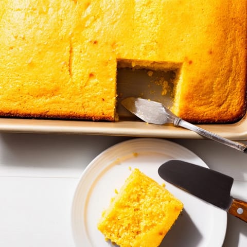 Freshly baked classic Cornbread with a golden-brown crust sits sliced on a wooden cutting board, ready to serve with honey butter.