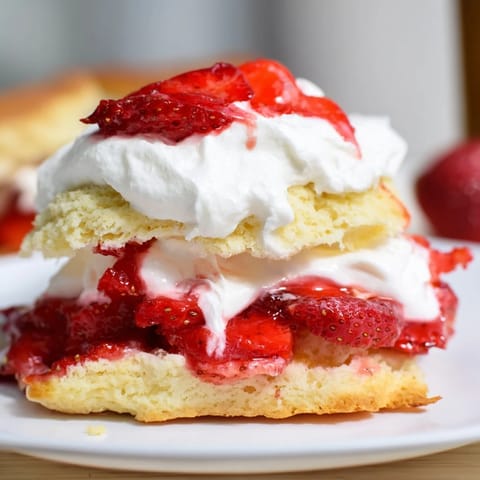 A close-up view of a plated Strawberry Shortcake dessert, drizzled with sweet strawberry syrup and topped with fresh mint leaves.