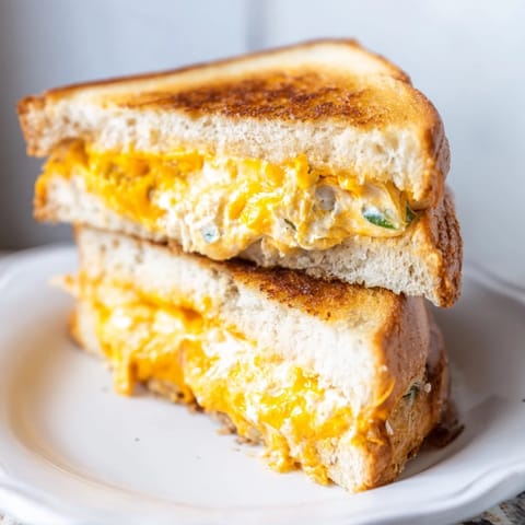 Two spicy jalapeño popper grilled cheese sandwiches sliced open to reveal creamy, cheesy filling with vibrant green pepper specks.  