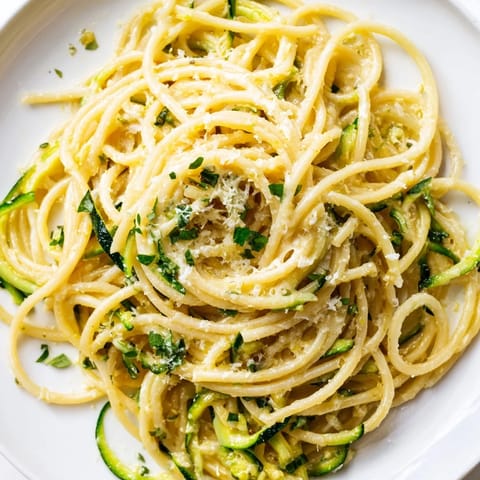 Close-up of lemon zucchini pasta featuring vibrant green zoodles, glossy butter sauce, and a light dusting of cheese.  