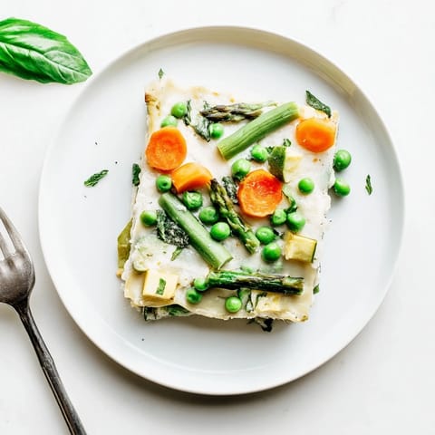 A close-up view of a slice of Spring Veggie Alfredo Lasagna reveals creamy ricotta and tender zucchini nestled between no-boil noodles.