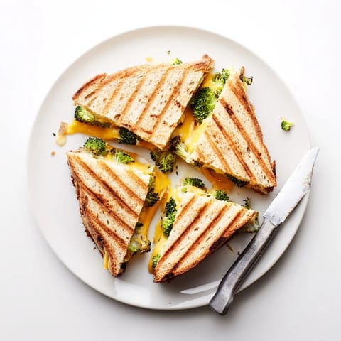 A close-up of Roasted Broccoli & Cheddar Grilled Cheese, showcasing golden, crispy sourdough and melted sharp cheddar oozing over tender, caramelized broccoli florets.