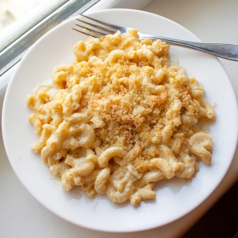 Close-up of a golden-brown baked macaroni and cheese casserole, bubbling with rich, gooey cheese and a crispy breadcrumb crust.