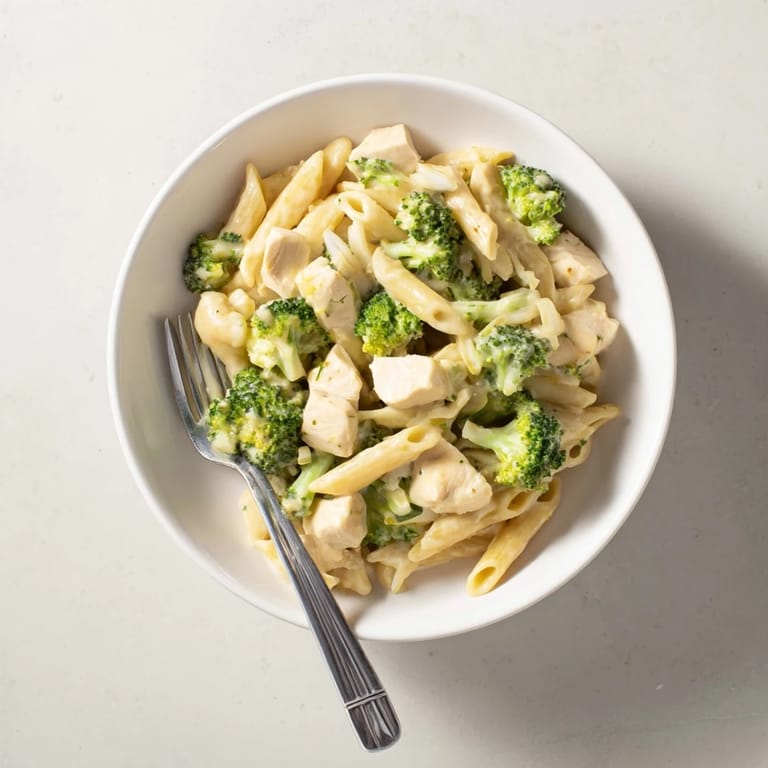 Tender penne pasta tossed with sautéed chicken, steamed broccoli, and a rich homemade cheddar cheese sauce in a white bowl.