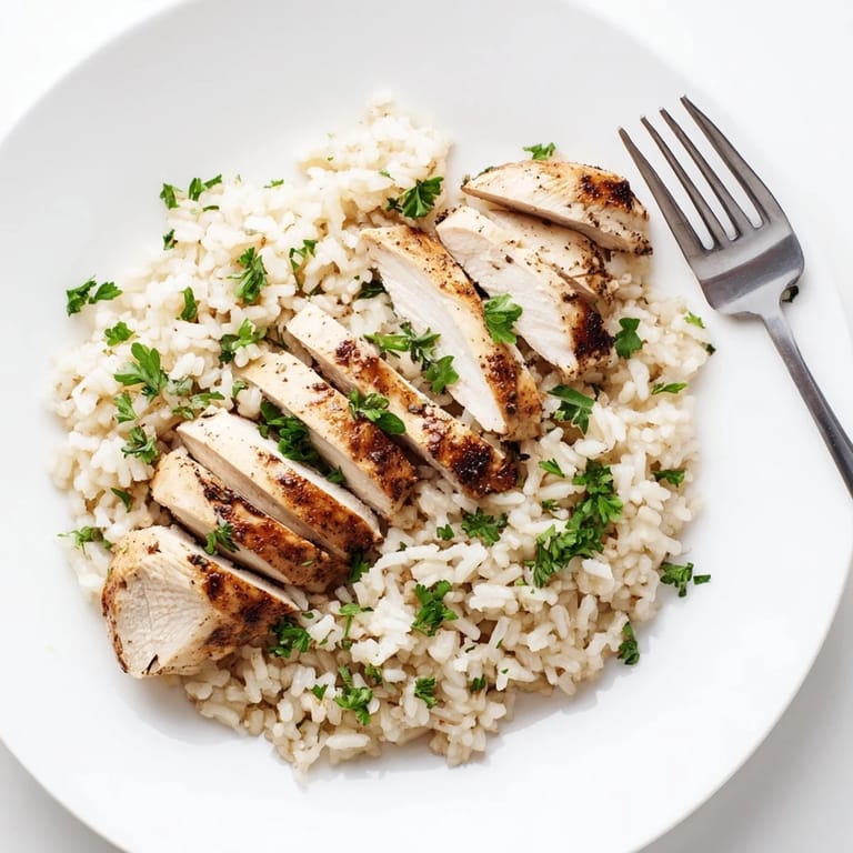 A close-up of tender sliced chicken resting on a bed of aromatic garlic butter rice, with a hint of steam rising from the fluffy grains.
