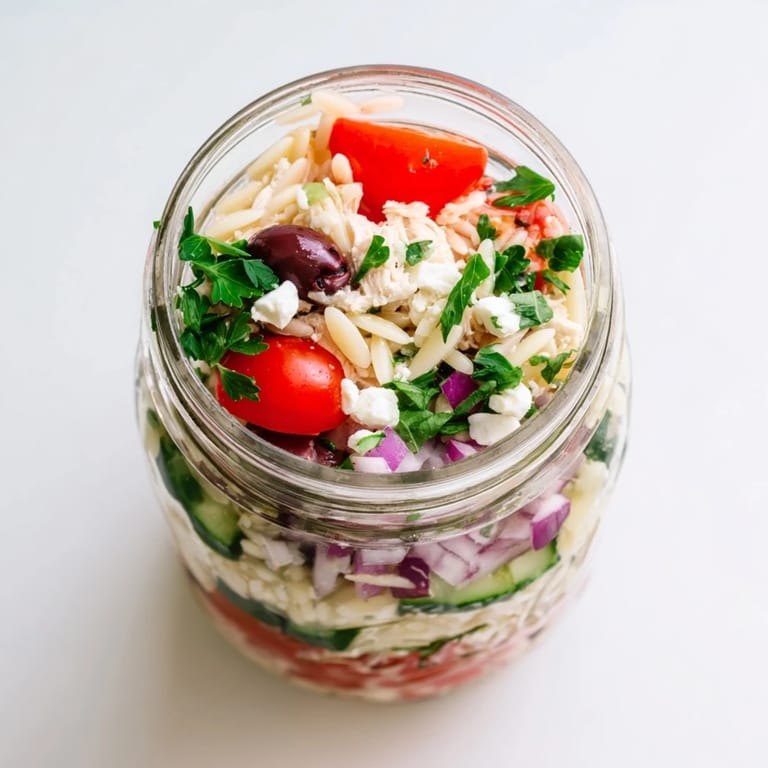 A refreshing grab-and-go lunch jar filled with Greek Pasta Chicken Salad, briny olives, creamy feta, and crisp Mediterranean vegetables.