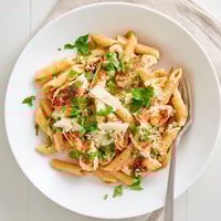 Creamy penne pasta tossed with tender honey chipotle chicken, fresh cilantro, and grated Parmesan, served warm in a white bowl.