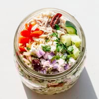 Layered Greek Pasta Chicken Salad Jars with orzo, diced grilled chicken, cherry tomatoes, cucumber, red onion, and Kalamata olives.